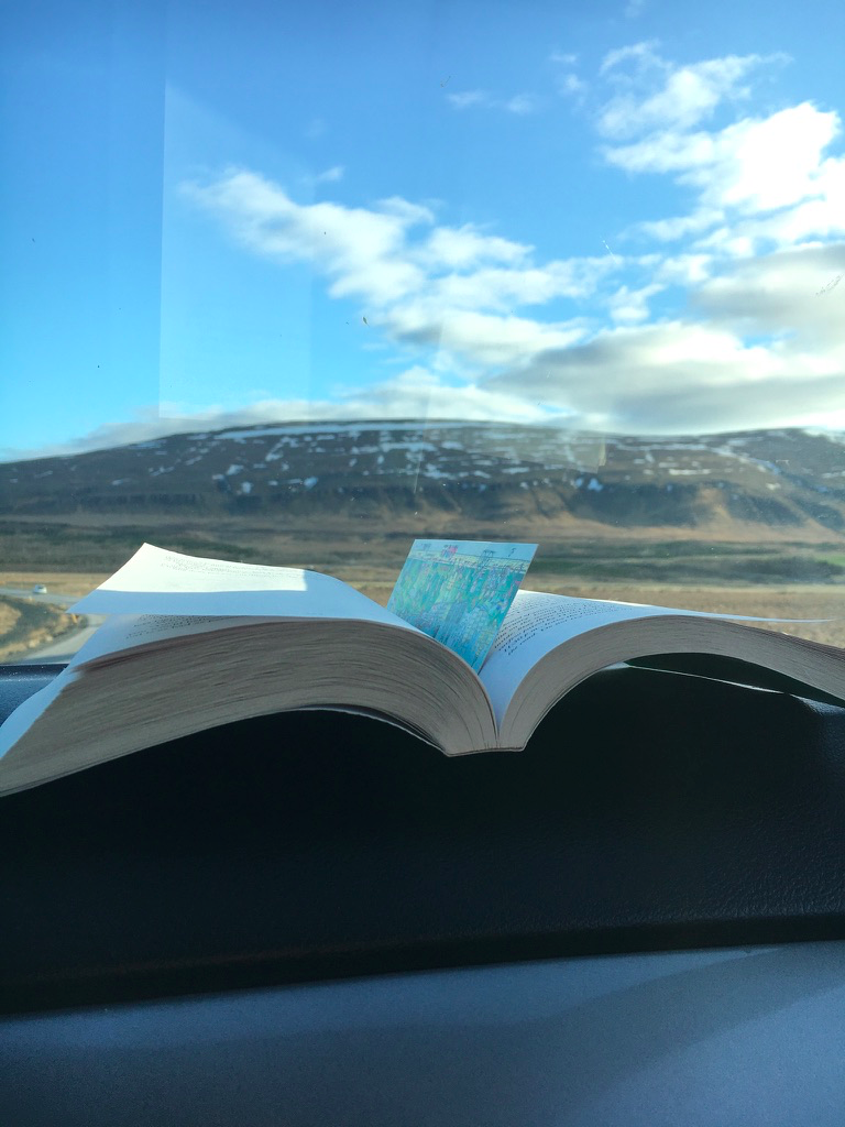 A book placed on the dashboard of a car with a scenic Icelandic landscape in the background
